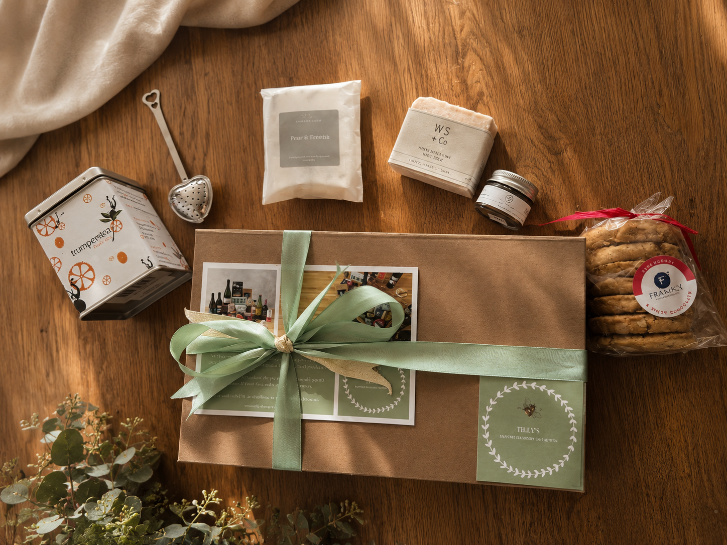 Gift box with green ribbon on a wooden table with tea bags and cookies.